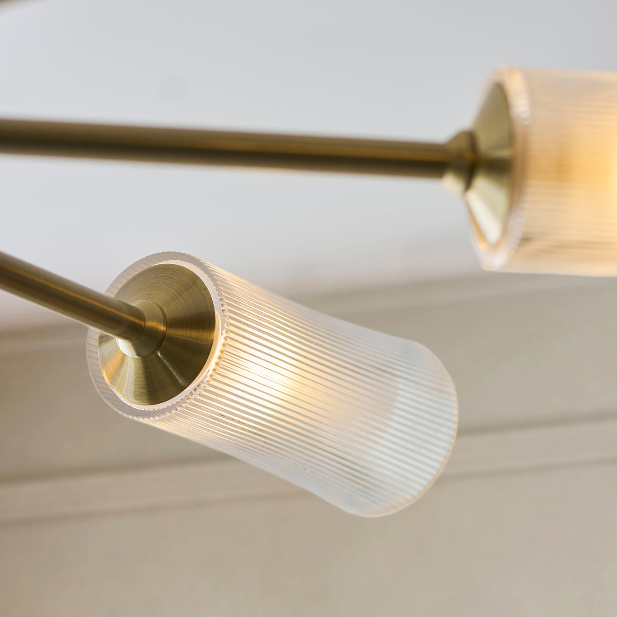 Detail of an Avelyn ribbed glass shade lit from within on its brass arm