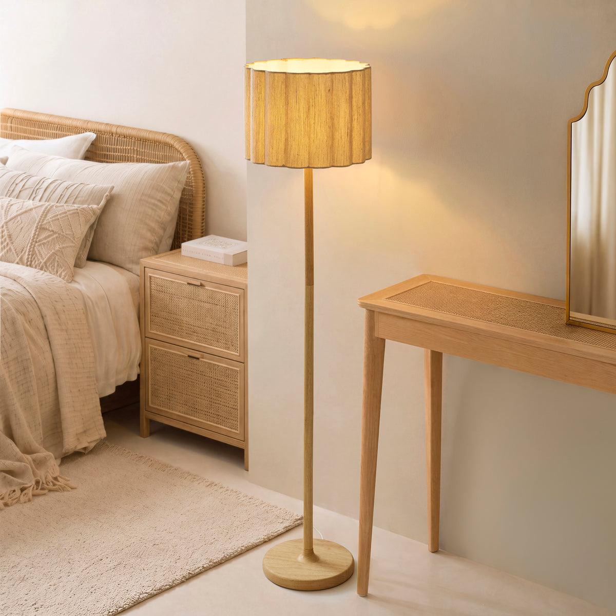 Olson oak floor lamp lit beside a rattan bed, cane bedside drawers and oak console table in a neutral bedroom