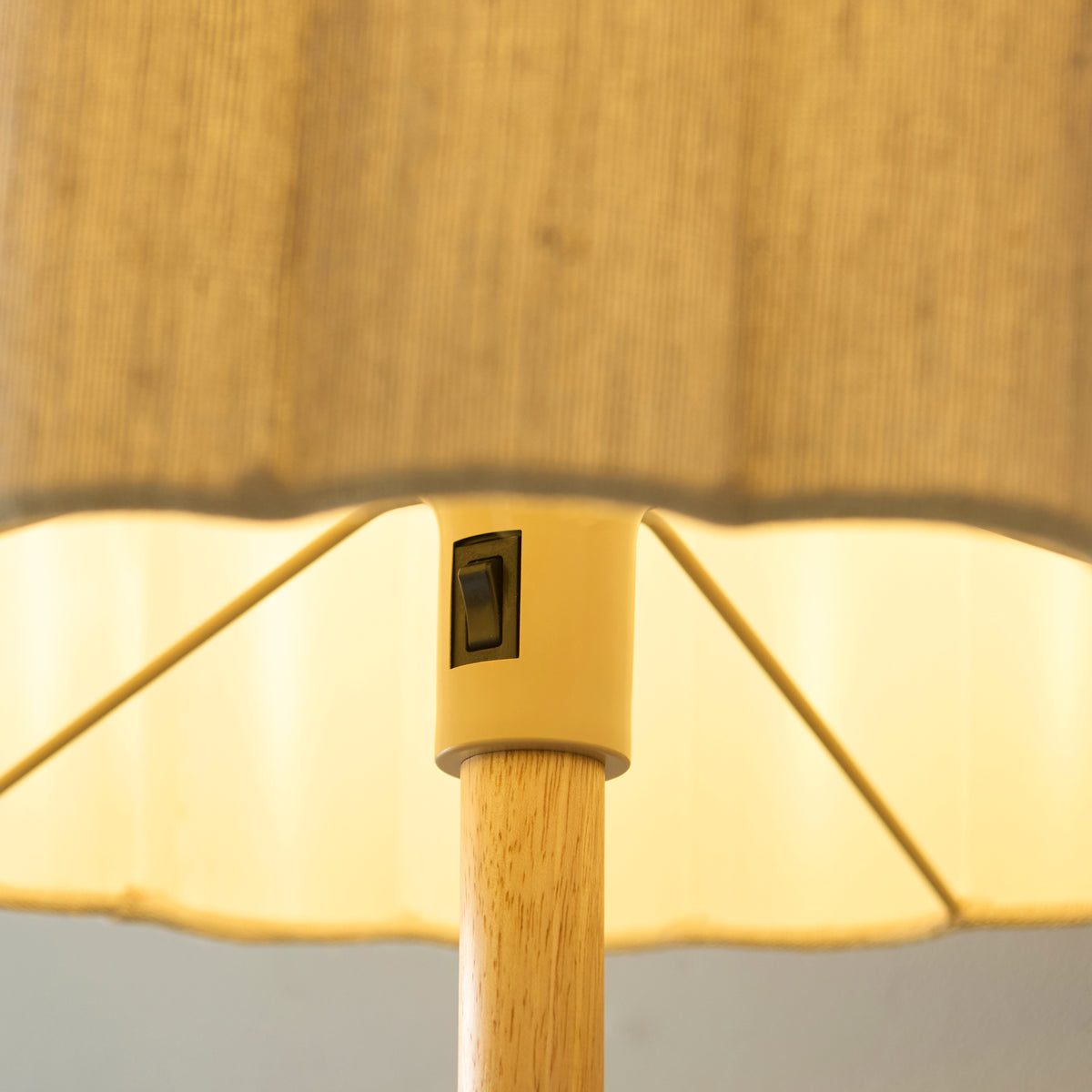Close-up of the Olson floor lamp's rocker switch and scalloped shade edge above the oak-stained stem