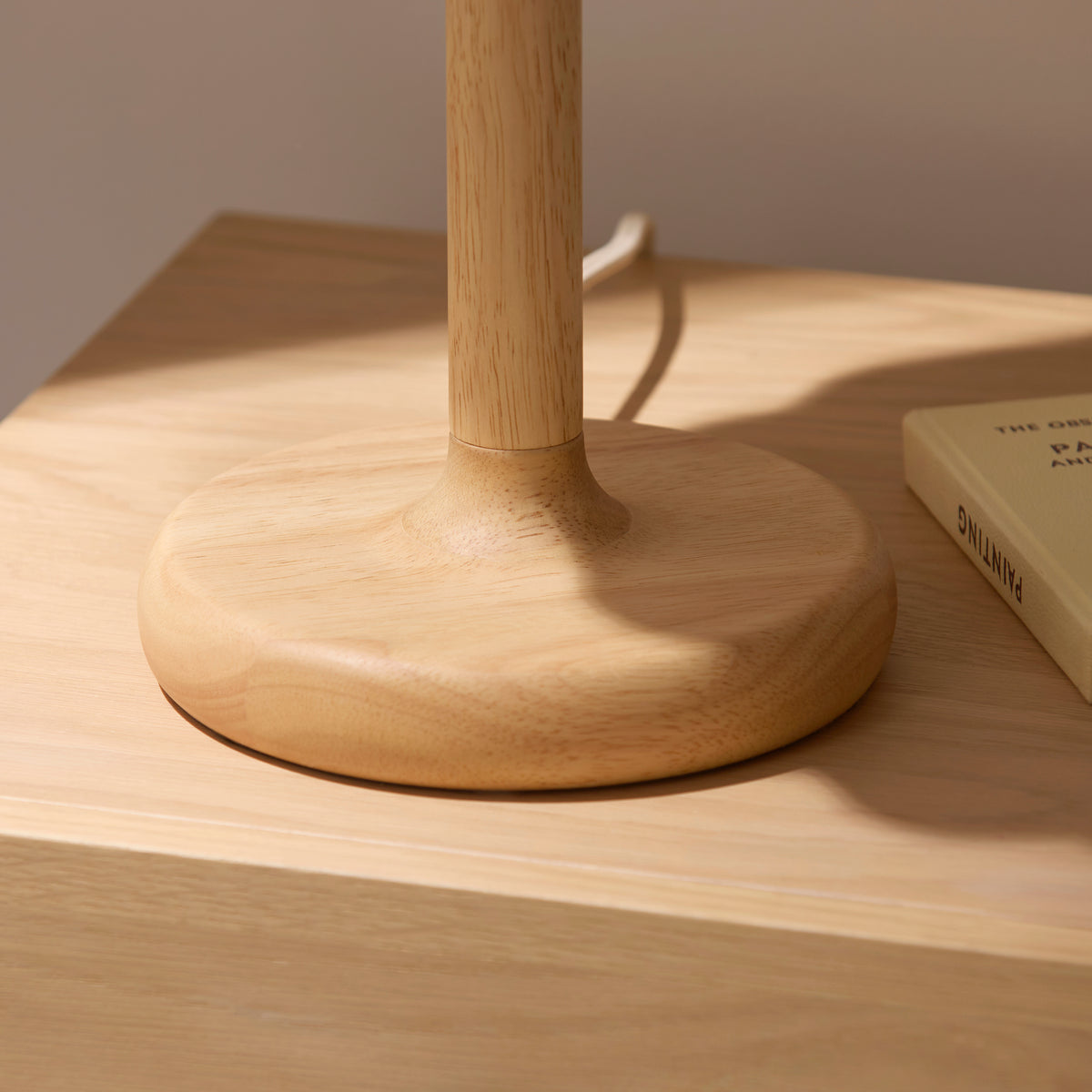 Oval oak base and stem of the Olson table lamp resting on an oak bedside table beside a book
