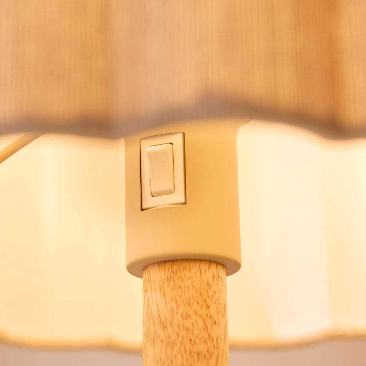 Detail of the Olson table lamp's cream rocker switch below the softly lit scalloped fabric shade