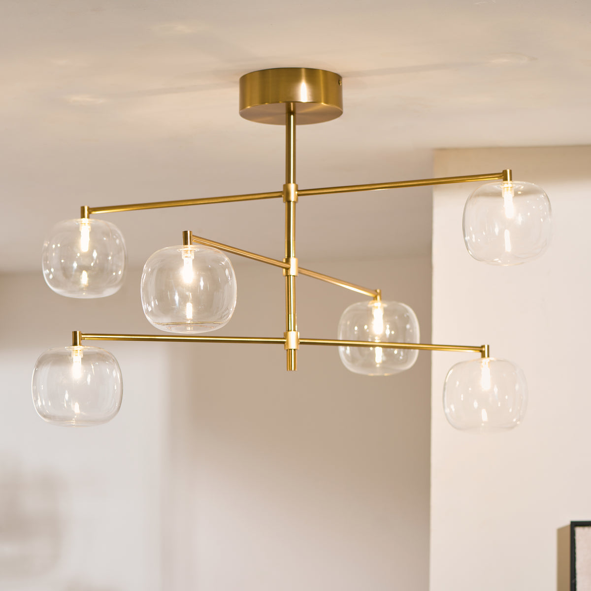 Oslo adjustable-arm brass pendant glowing with six clear glass globe shades in a neutral room