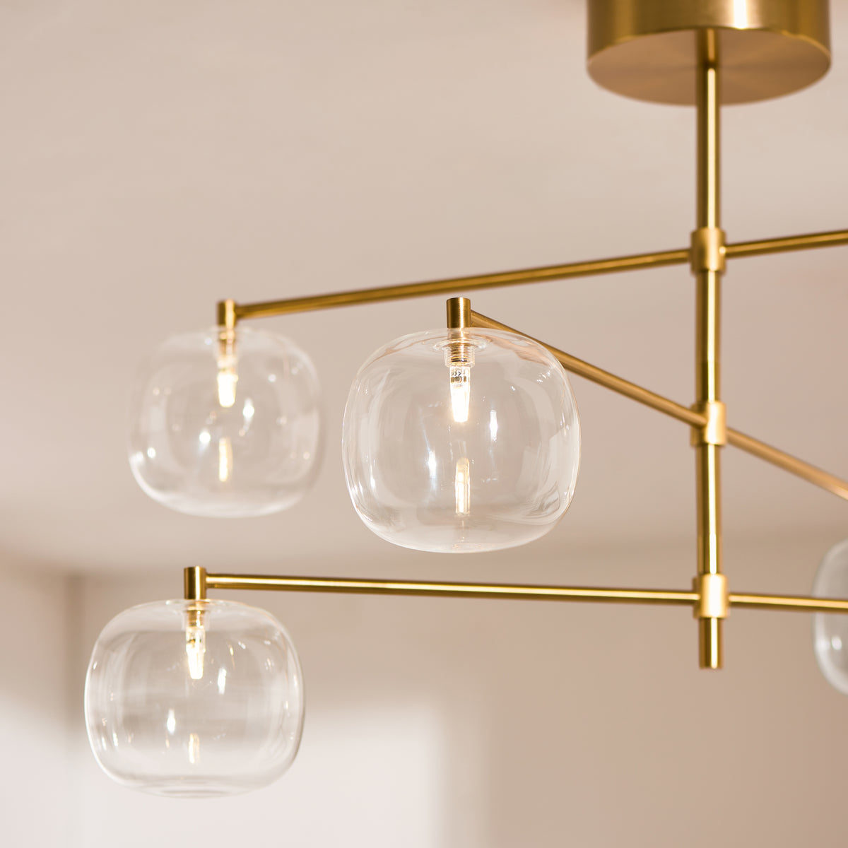 Close-up of the Oslo pendant's clear glass globes and brushed brass arms with lit bulbs