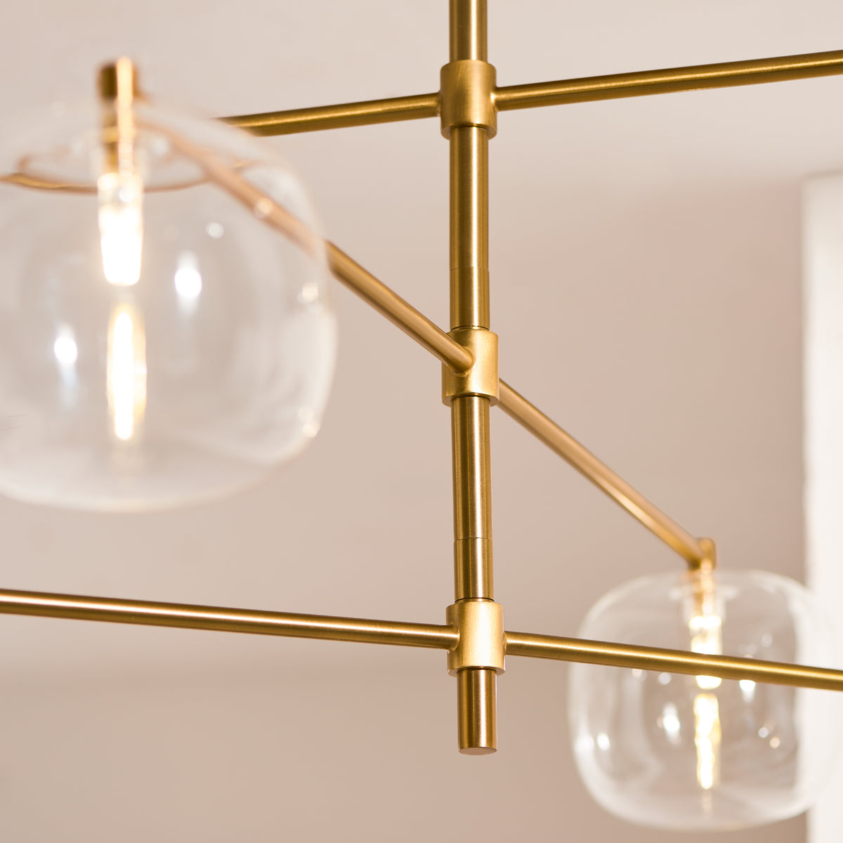 Brushed aged brass crossed arms and joints of the Oslo pendant against a pale ceiling