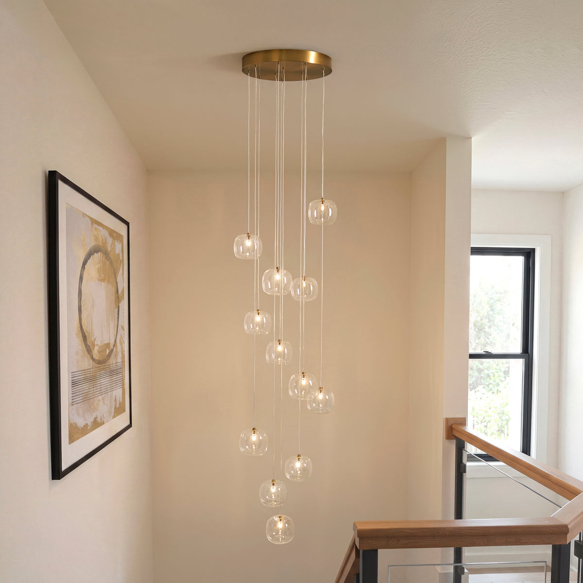 Oslo cascade pendant lit in a stairwell with framed print, oak handrail and glass balustrade