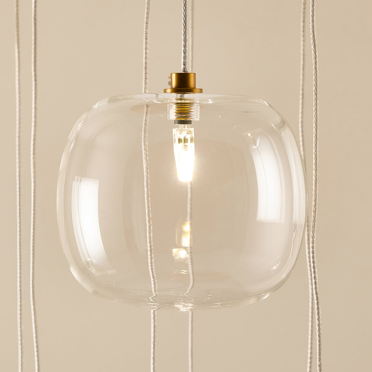 Close-up of one clear glass globe and brass lampholder on the Oslo cascade pendant