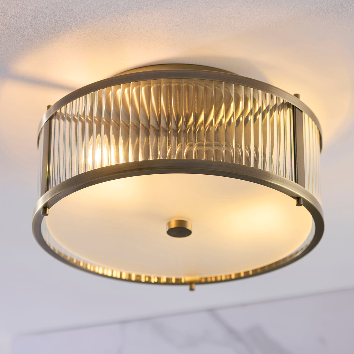 Ridgeton flush ceiling light seen from below with ribbed glass surround and glowing opal base