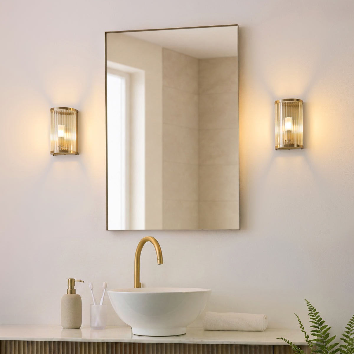 Pair of Ridgeton brass wall lights lit either side of a bathroom mirror above a round basin