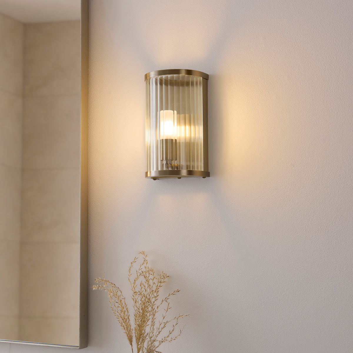 Ridgeton brass wall light casting warm up and down light next to a framed bathroom mirror