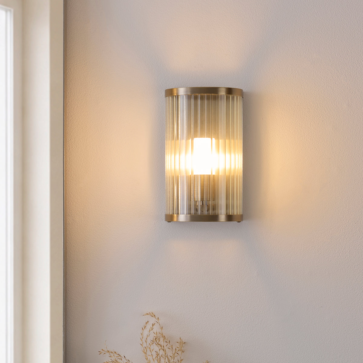 Ridgeton ribbed glass wall light glowing softly beside a window in a neutral bathroom