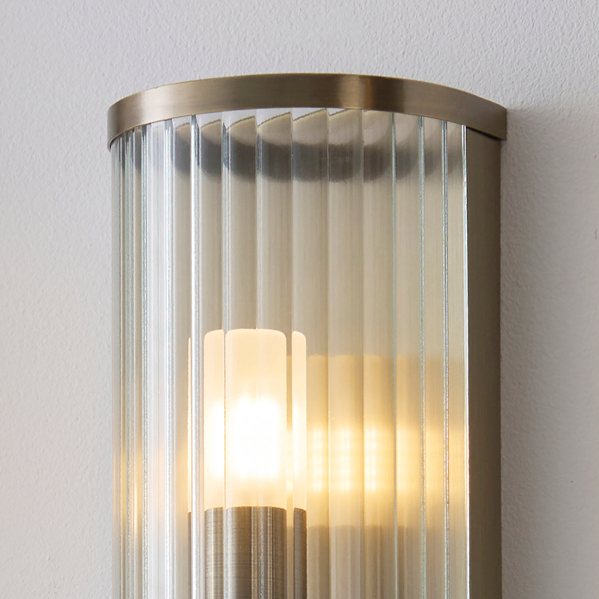 Detail of the lit opal cylinder inside the Ridgeton wall light's ribbed clear glass shade
