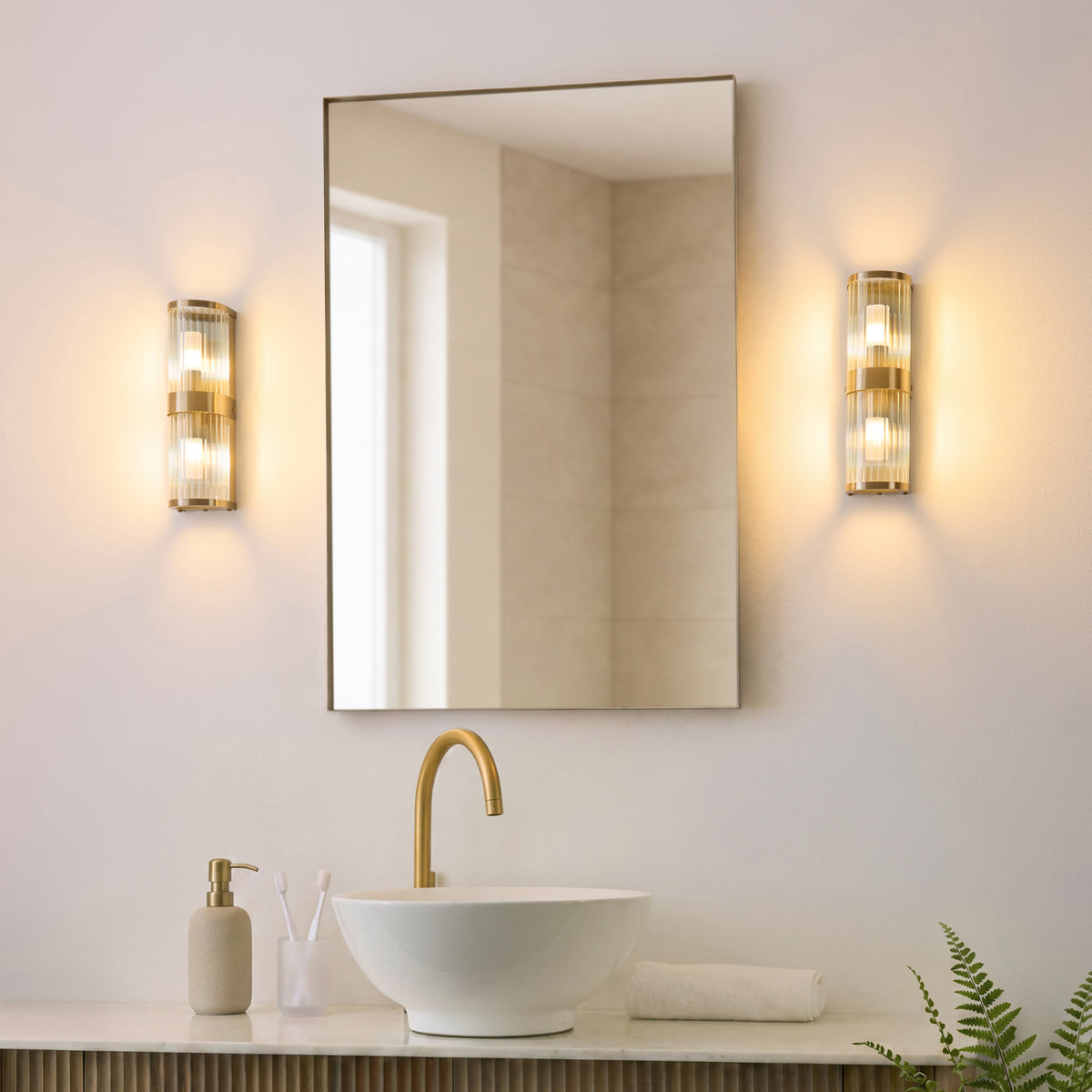 Pair of Ridgeton brass bathroom wall lights flanking a mirror above a round basin and brass tap