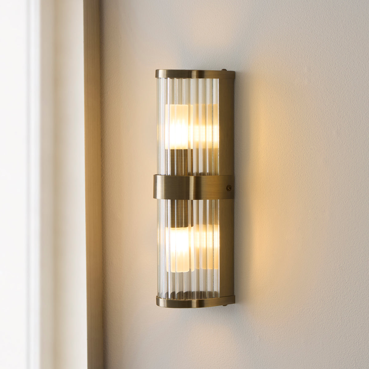 Angled view of the Ridgeton antique brass wall light with two frosted lamps behind ribbed glass