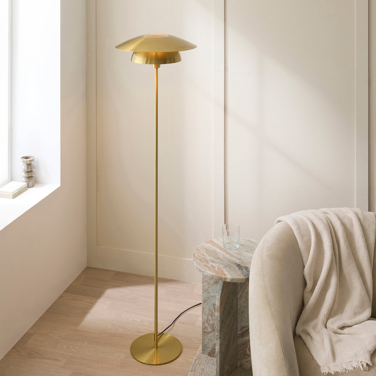 Lyon satin brass floor lamp glowing in a bright panelled living room beside a throw-draped sofa