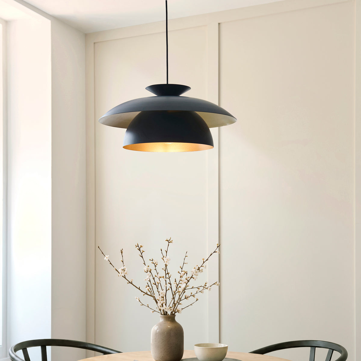Lyon black and brass pendant glowing over an oak dining table in a panelled room