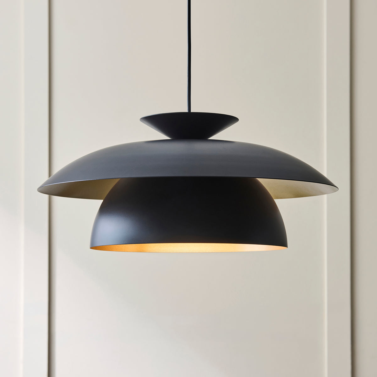 Lyon pendant's tiered matt black shades with brass-toned interior against panelled walls