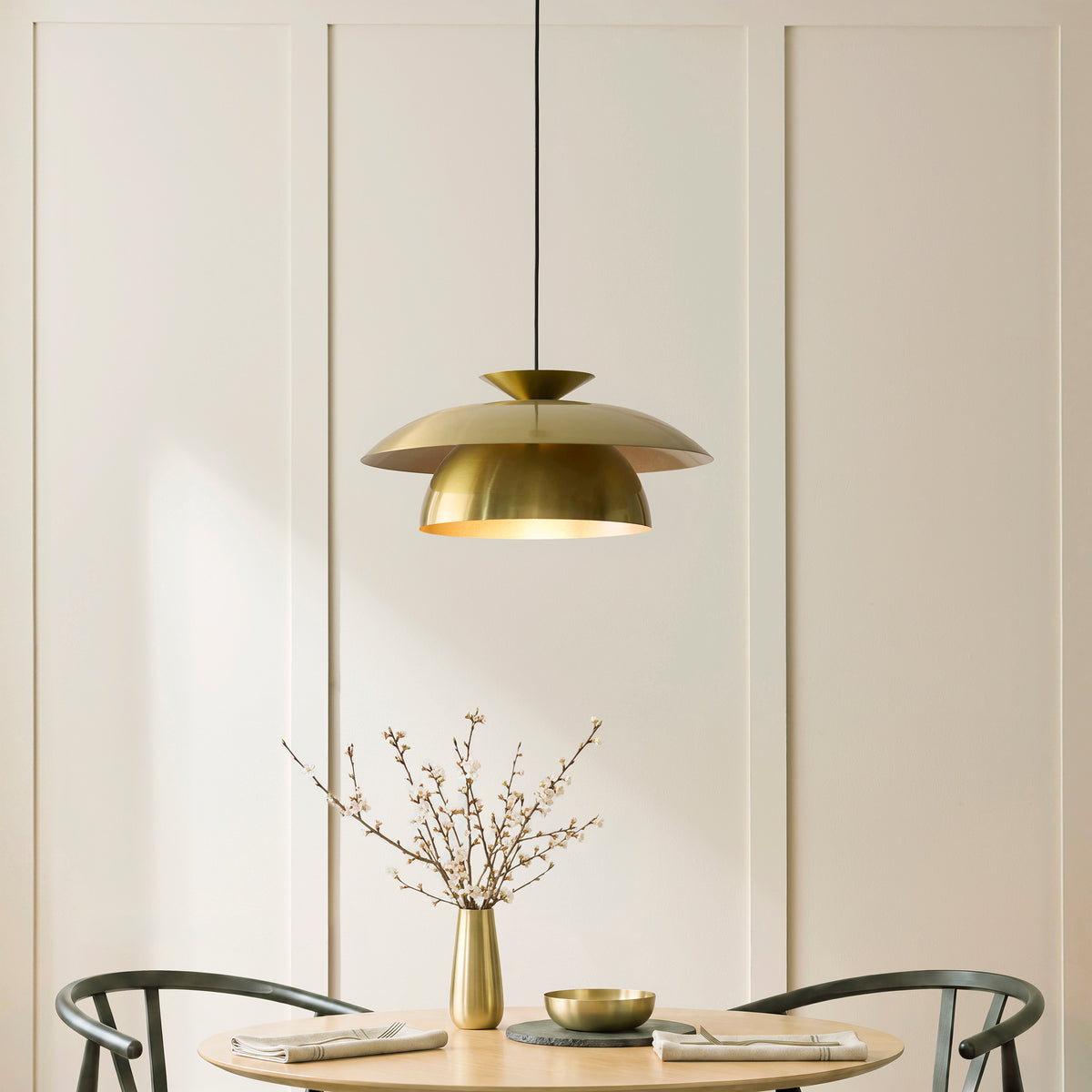 Lyon brass pendant lit above a round dining table with blossom vase and dark wood chairs