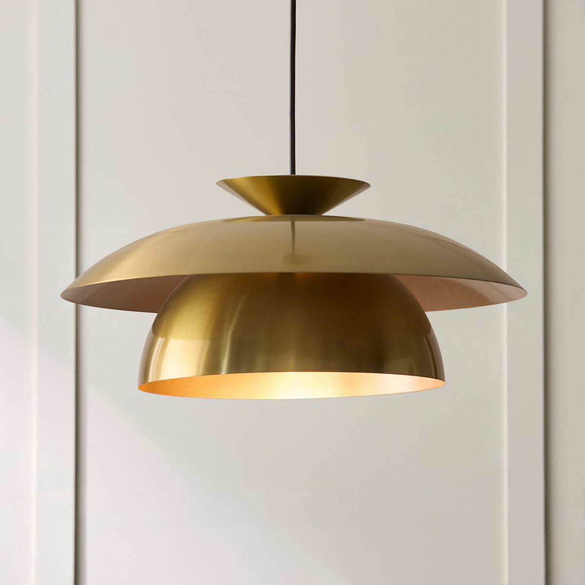 Layered brushed brass shades of the Lyon pendant seen close against pale panelling