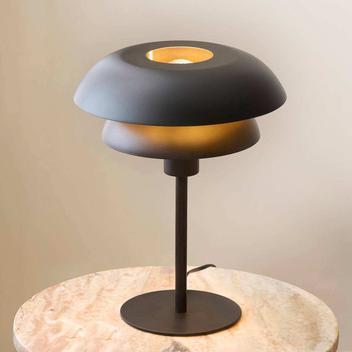 Close-up of the Lyon table lamp's tiered black shades with warm brass-lined glow