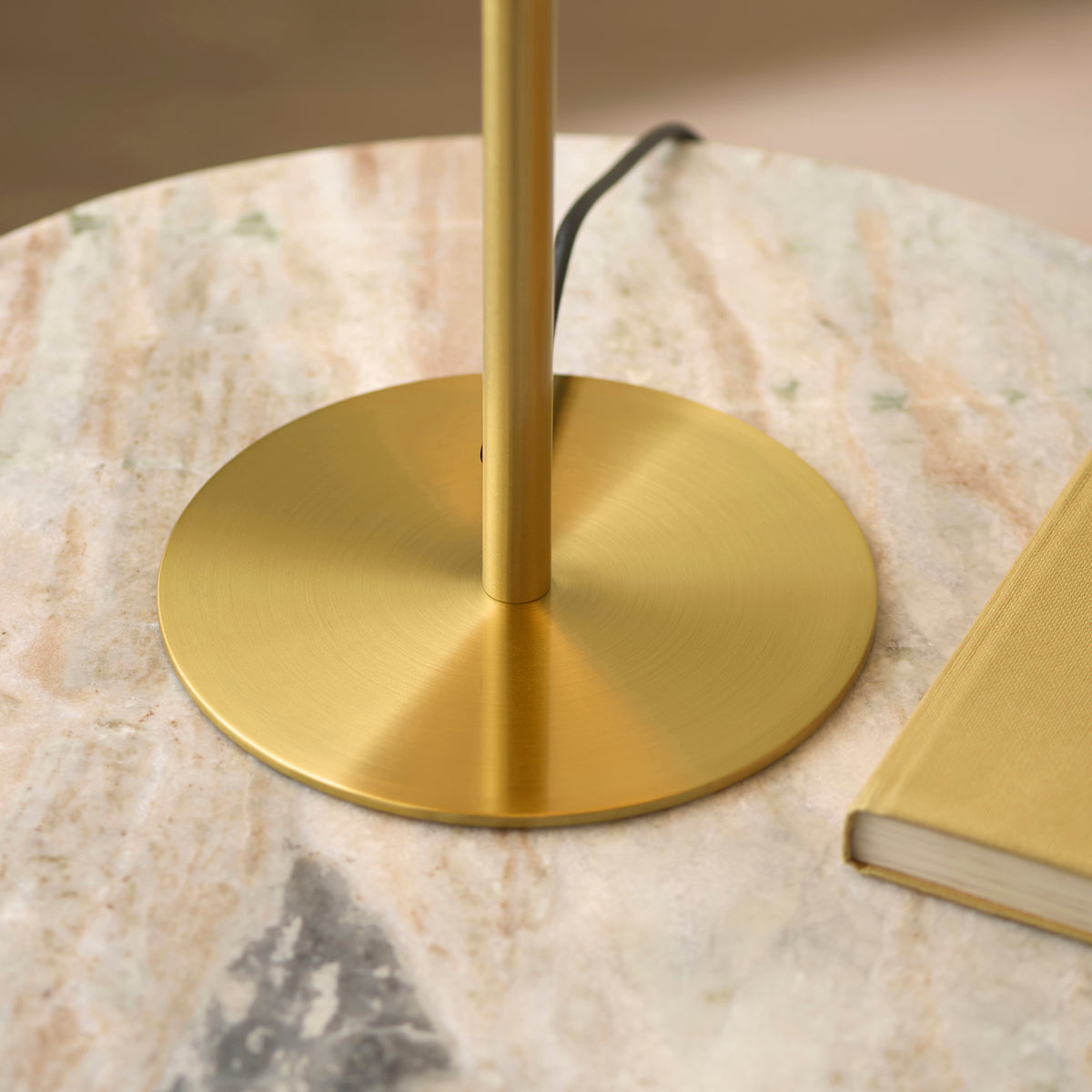 Brushed brass disc base of the Lyon table lamp on a marble surface beside a book