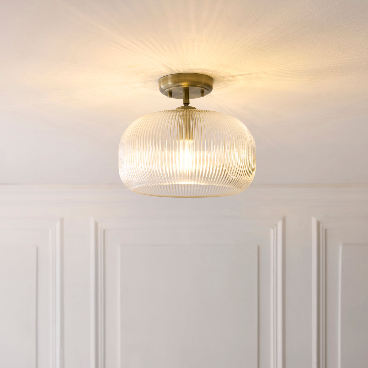 Harborne ribbed glass flush ceiling light lit against a white panelled wall and ceiling