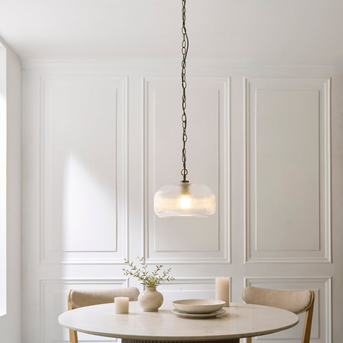 Harborne ribbed glass pendant lit above a round dining table with vase, candles and pale panelled walls
