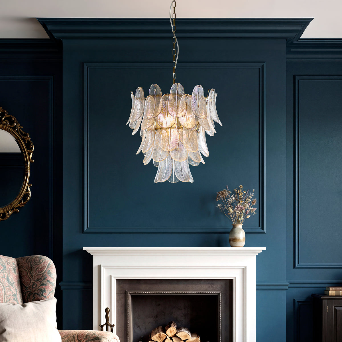 Autumn glass leaf chandelier lit above a white fireplace in a dark blue panelled living room