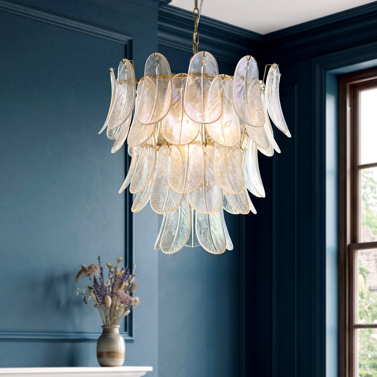 Autumn tiered leaf-glass chandelier glowing in a navy panelled room beside a window and lavender vase