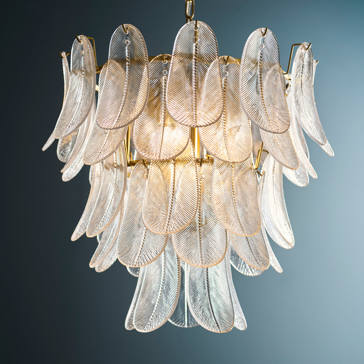 Autumn chandelier's layered textured glass leaves and aged brass frame against a deep blue wall