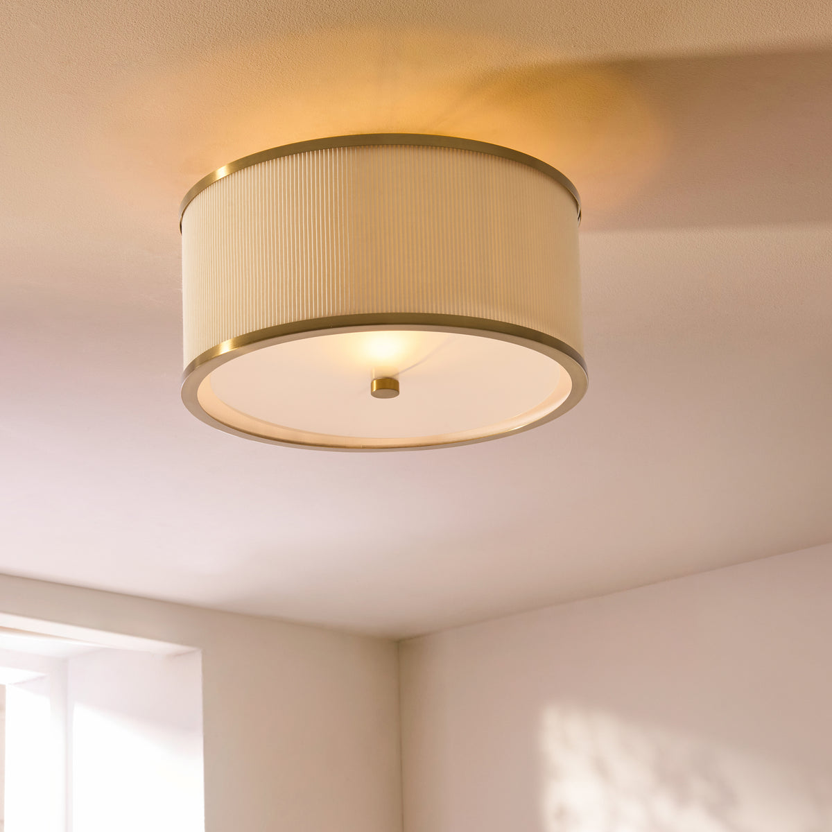 Lexi flush ceiling light lit on a white ceiling, its ivory pleated shade casting a warm glow