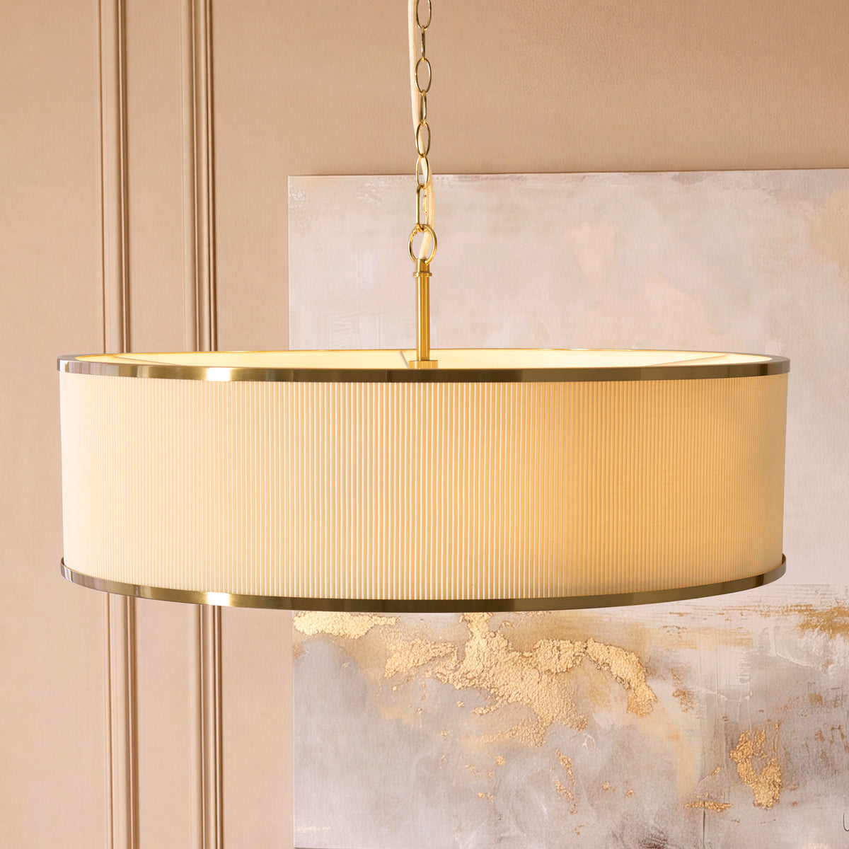 Lexi pendant's pleated ivory shade and brass rims lit in front of a gold-flecked canvas