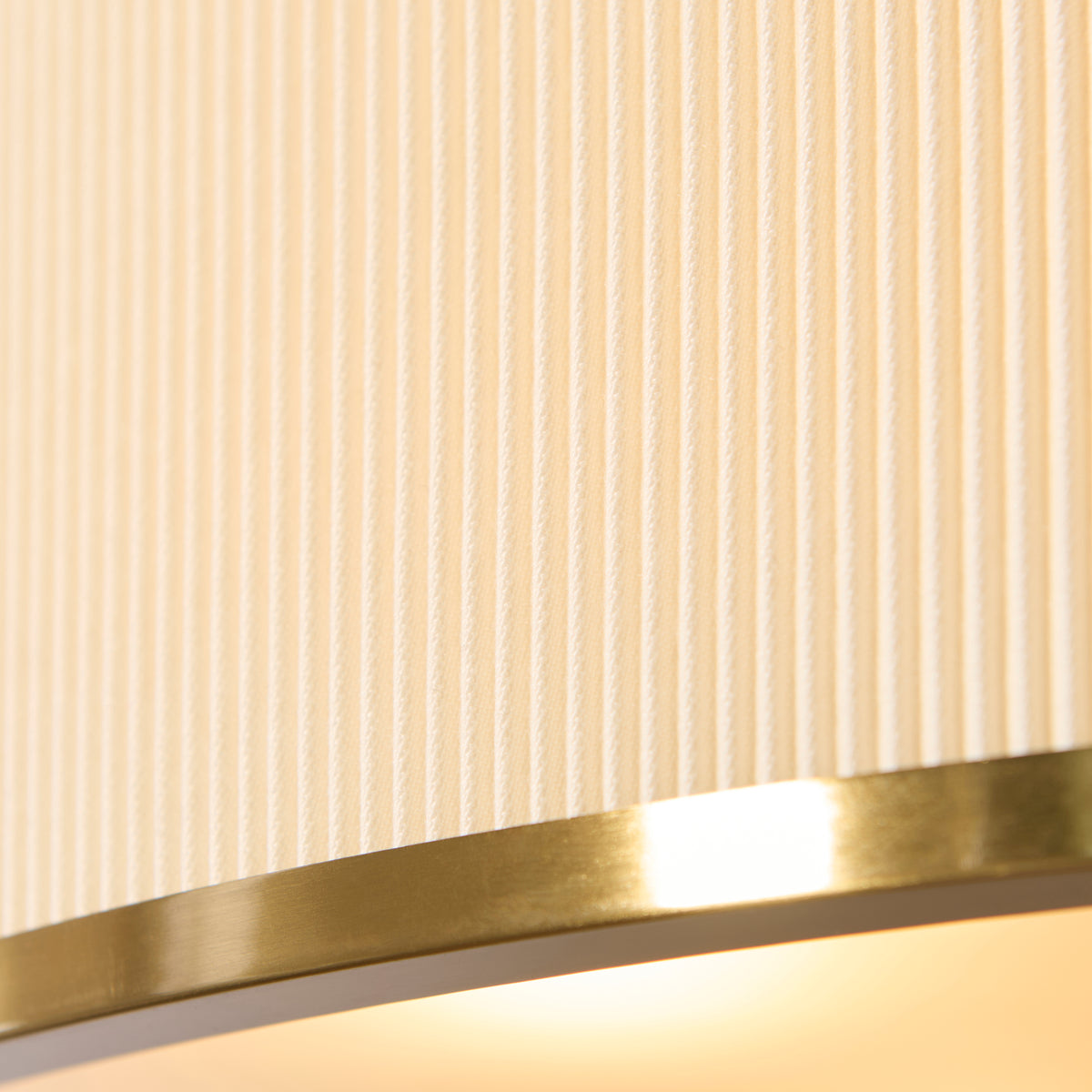 Macro detail of the ivory pleated fabric and brushed brass rim on the Lexi pendant shade