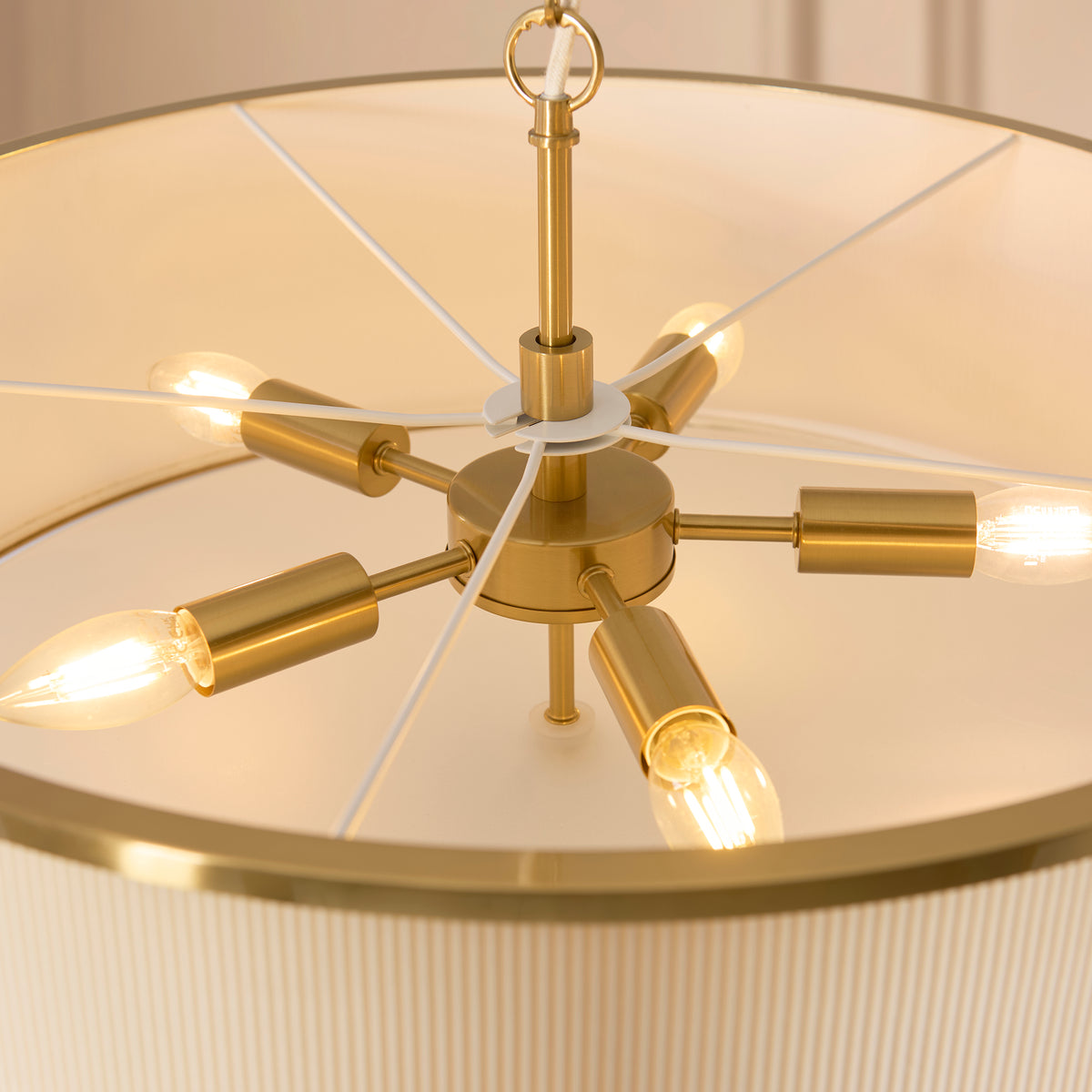 Five brass lamp holders with candle bulbs inside the ivory pleated Lexi pendant shade