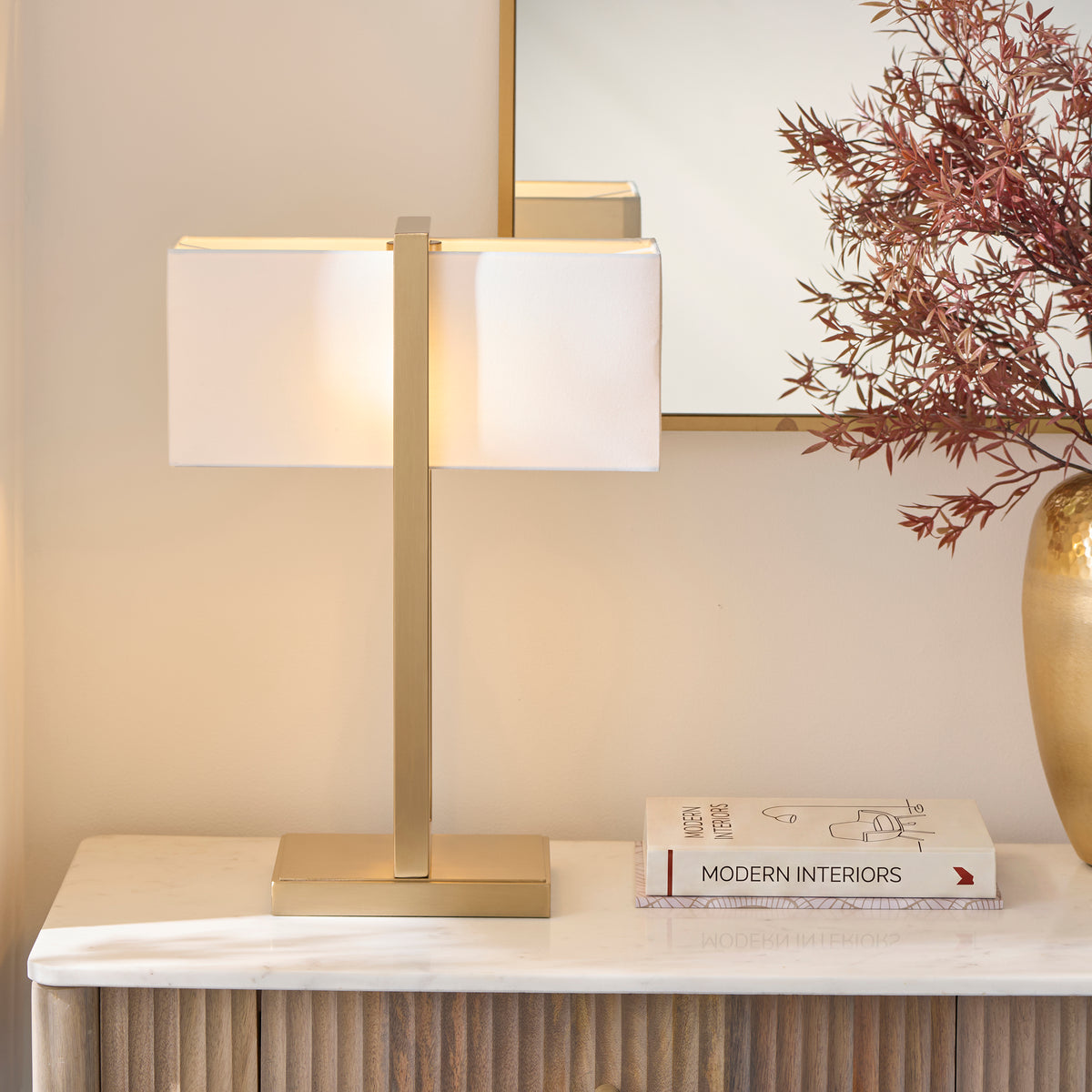 Angled view of the Seattle brass table lamp on a marble console beside a vase of autumn foliage