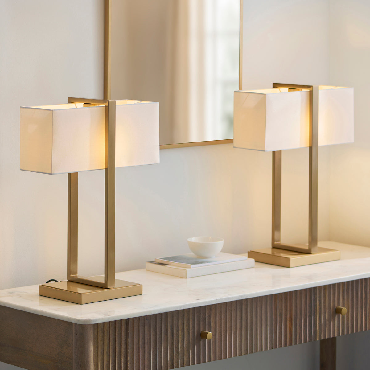 Pair of lit Seattle brass table lamps on a fluted console table with a mirror above