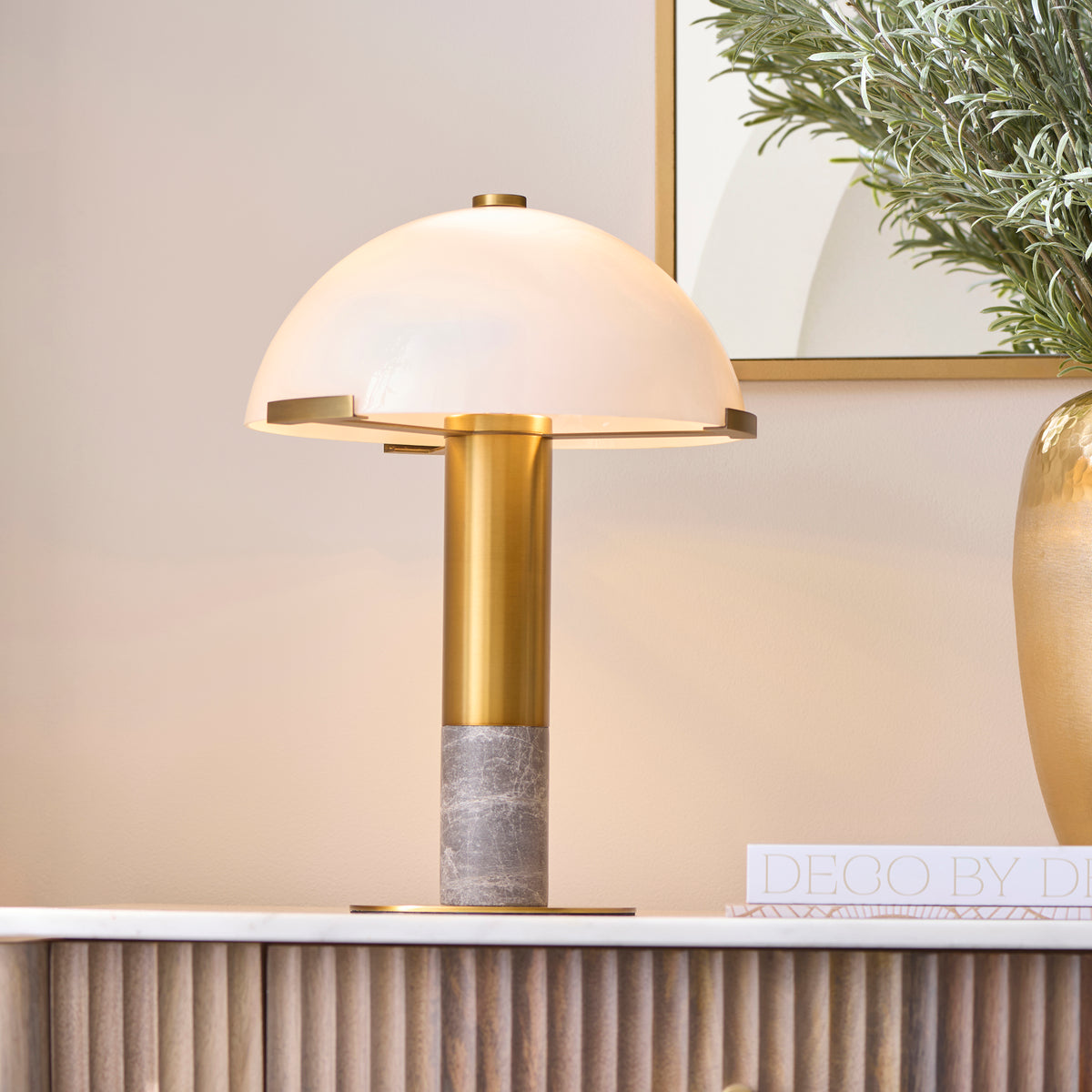 Lit Hansel lamp with domed opal glass shade on a marble worktop with olive foliage nearby