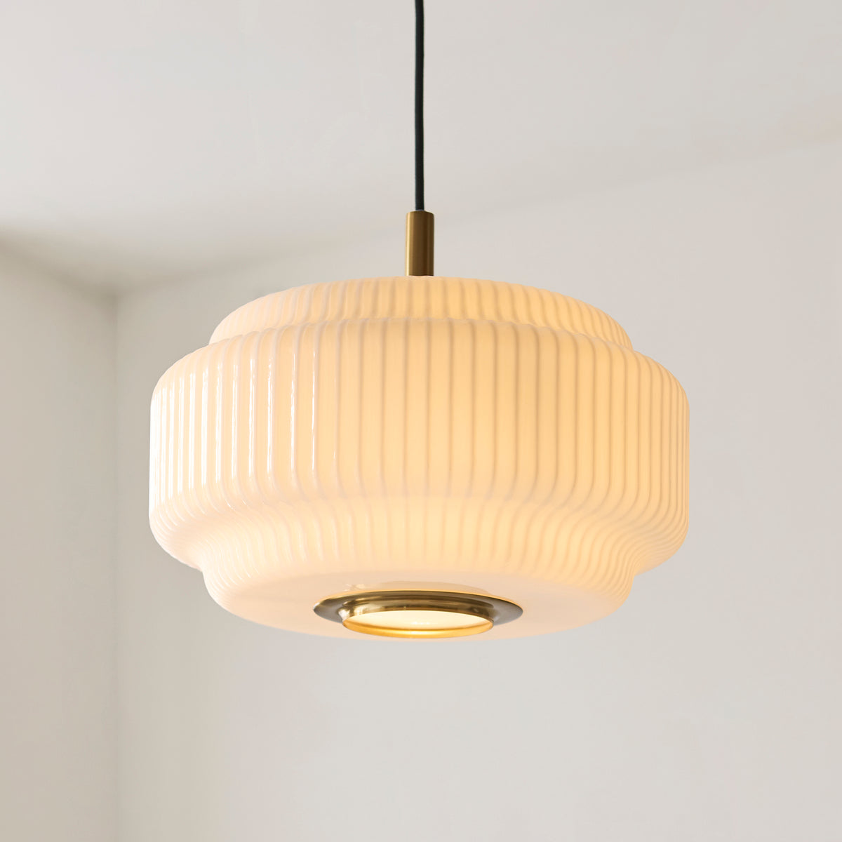 Lit Evora pendant showing its tiered ribbed opal glass shade and brass diffuser ring