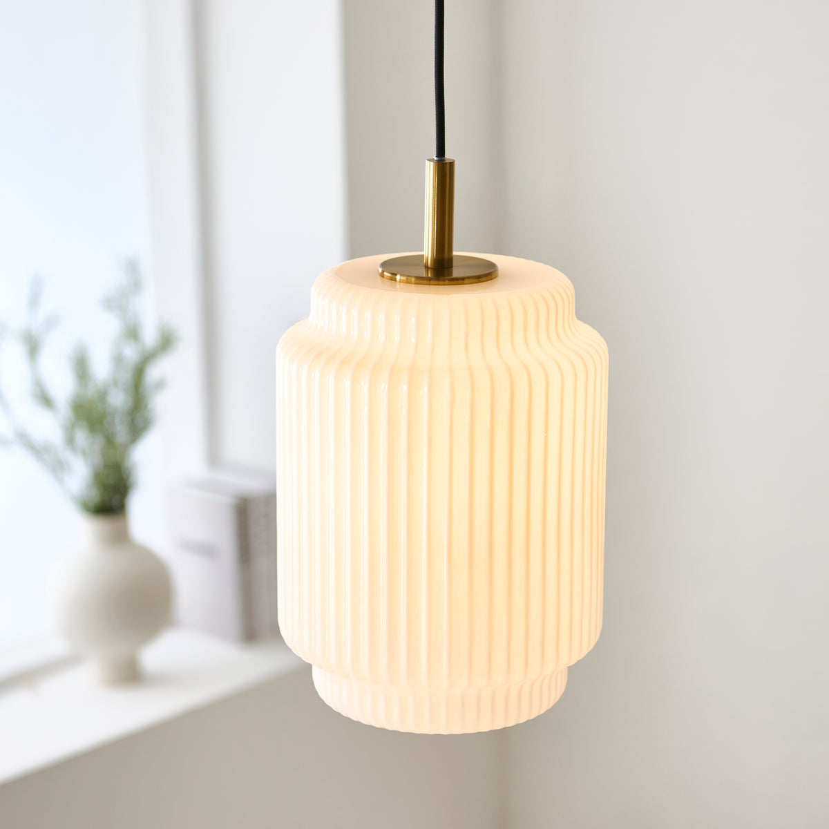 Evora ribbed glass pendant glowing softly in a bright room with a vase on the windowsill