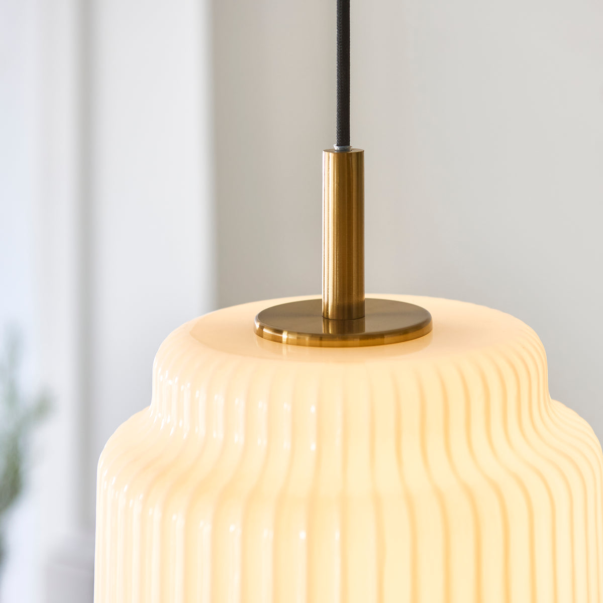 Detail of the Evora pendant's aged brass stem and cap on the ribbed opal glass shade