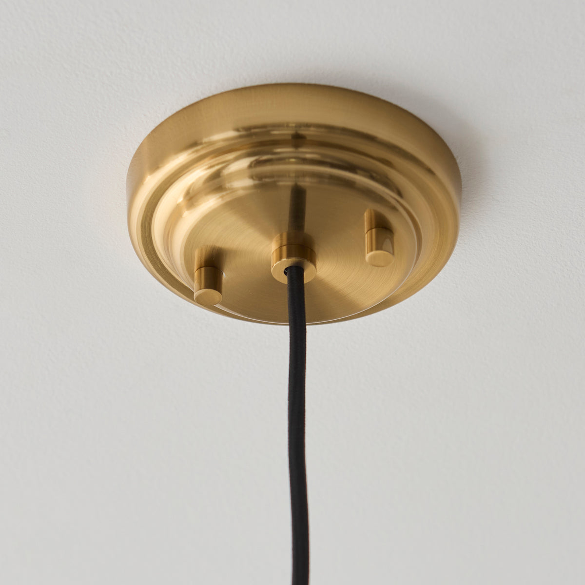 Aged brass ceiling rose and black flex of the Evora pendant against a white ceiling