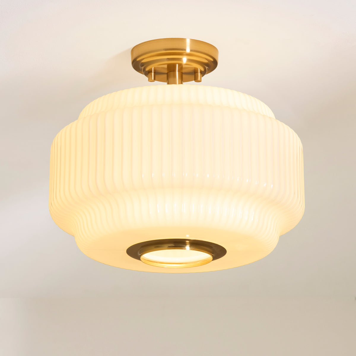 Lit Evora flush ceiling light showing its stepped ribbed opal glass shade and brass ring