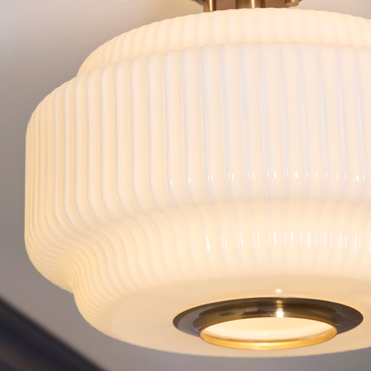 Close-up of the Evora ceiling light's ribbed opal glass and glowing brass-rimmed diffuser