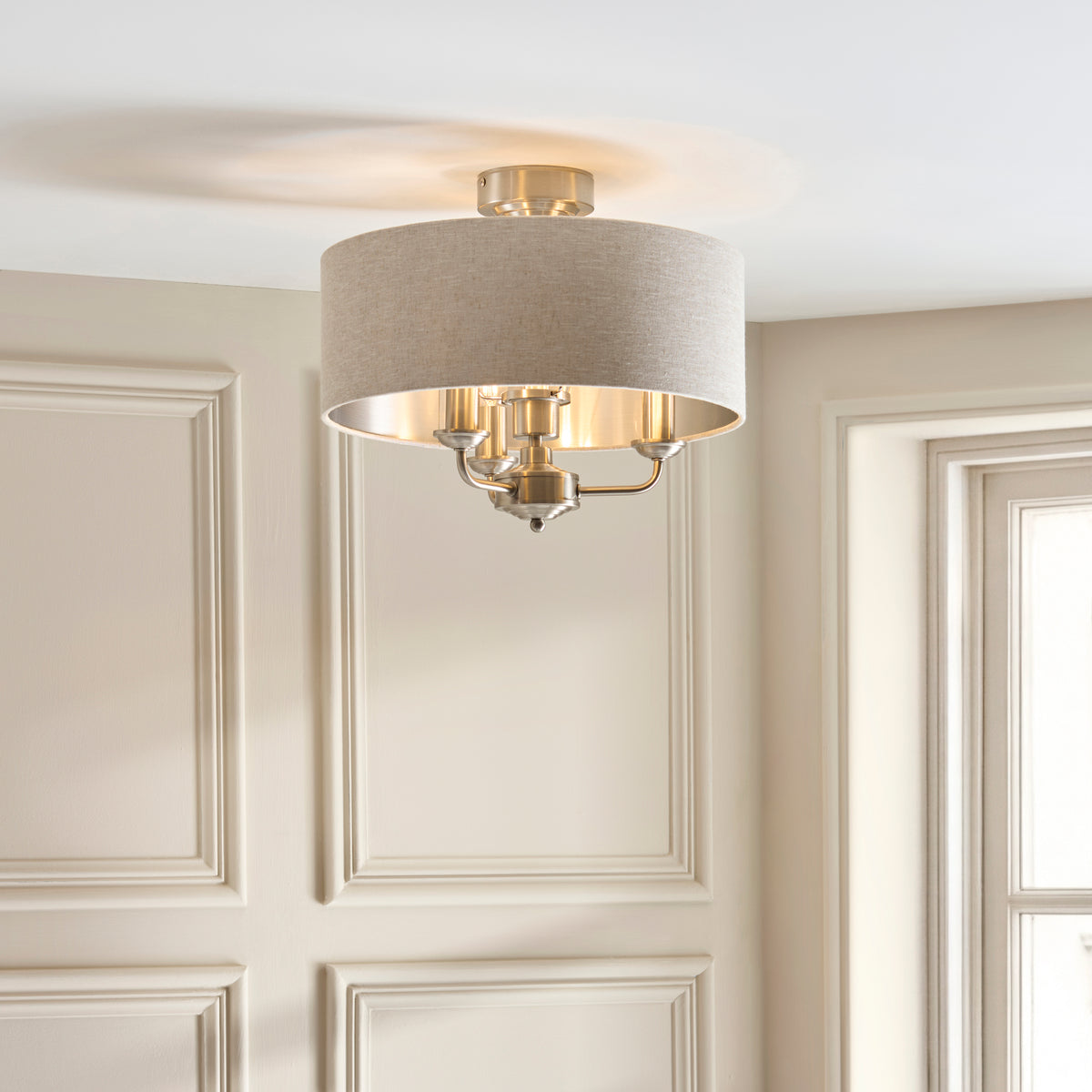 Highclere linen drum flush light glowing against a panelled wall in a cream hallway