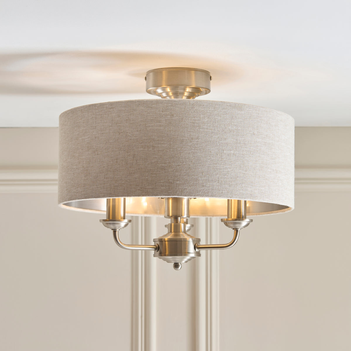 Angled view of the Highclere flush light's linen drum shade and chrome three-arm fitting