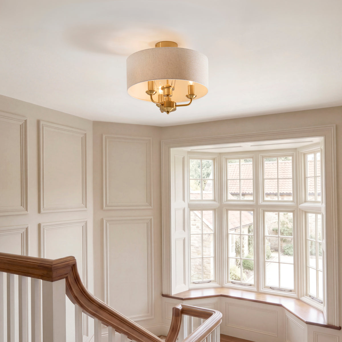 Highclere brass flush ceiling light lit above a panelled stairwell with a bay window