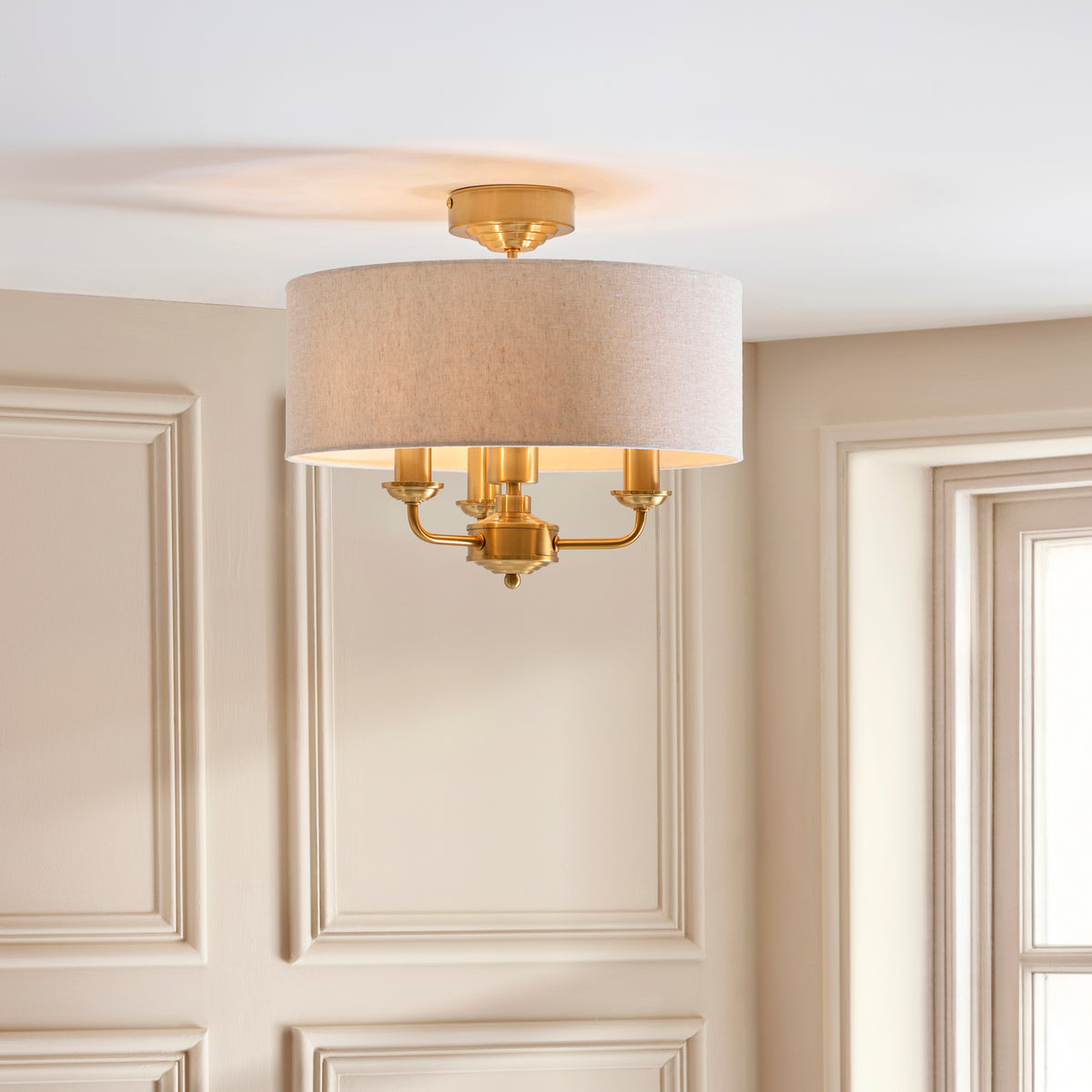 Highclere flush light with linen drum shade and brass arms against a panelled wall