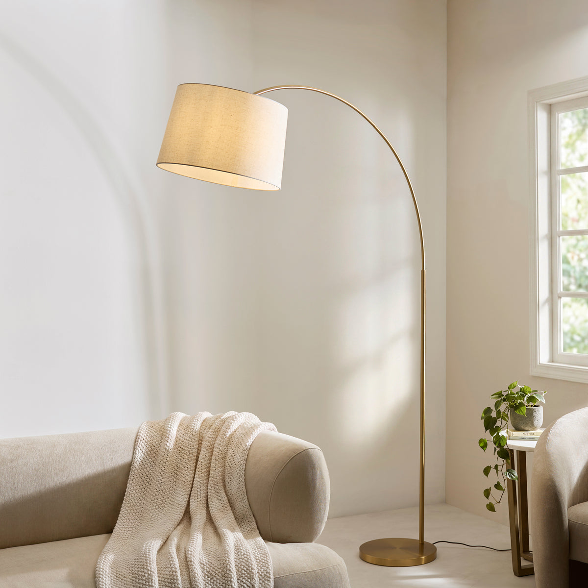 Carlson XL arched floor lamp curving over a pale sofa with a knitted throw in a bright room