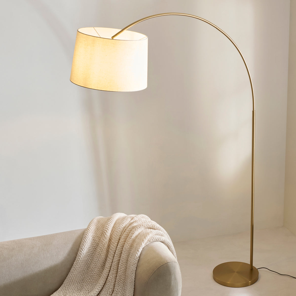 Carlson XL arc lamp's linen shade angled above a cream sofa with a chunky knit throw