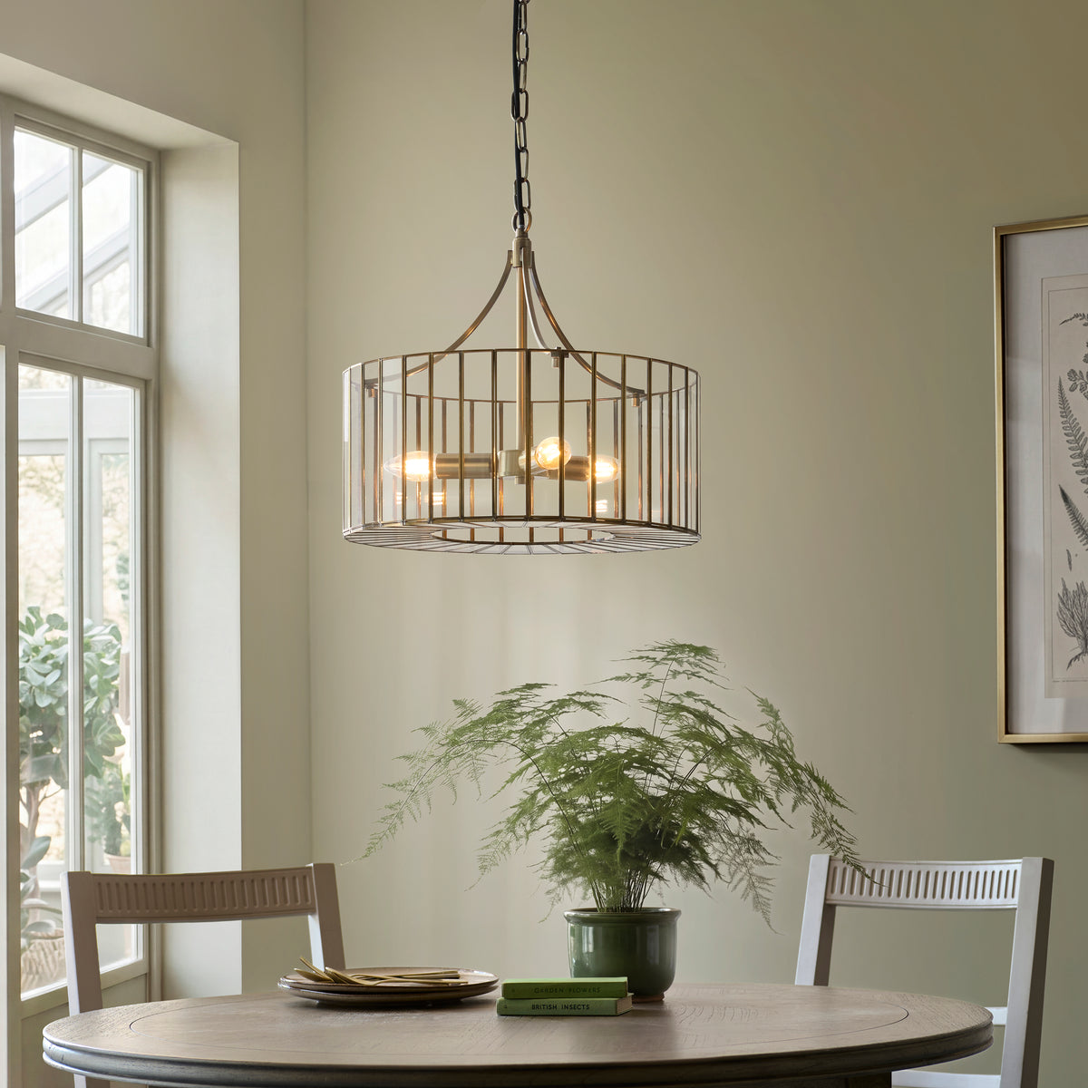 Antalya brass cage pendant above a round dining table with fern plant in a sage green dining room