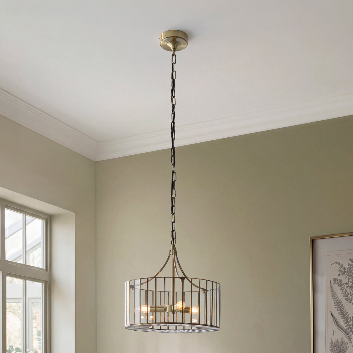 Antalya antique brass pendant hanging from a corniced ceiling in a sage green room